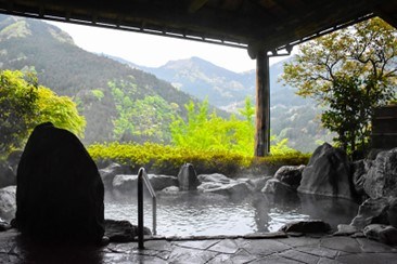 een warm Japans bad, buiten, onder een afdak, met uitzicht op de bergen en bossen